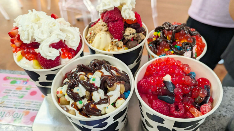 five cups of froyo with a variety of toppings, drizzles, and whipped cream