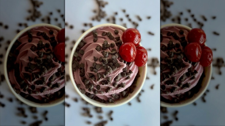 paper cup of reddish pink froyo with chocolate chips and three cherries