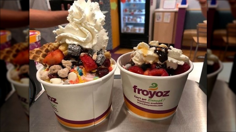 two cups of froyo with a ton of different toppings and piled high with whipped cream