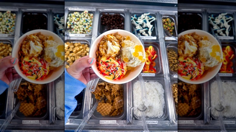 hand holding cup of yogurt over toppings bar