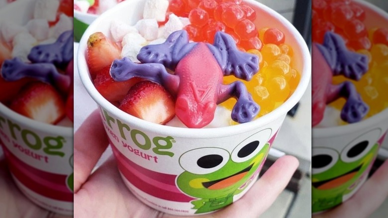 cup of froyo with fun toppings like fresh strawberry chunks, boba, coconut, and a gummy frog