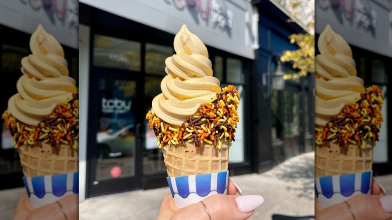 a waffle cone of orange froyo with brown, orange, and yellow sprinkles