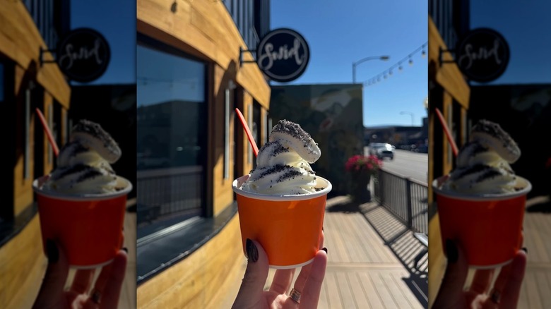 orange cup of white froyo with a dusting of oreos and an orange plastic spoon dipped in it