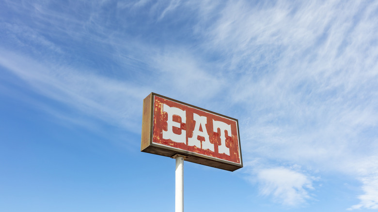 Roadside restaurant sign says eat in all capital letters against blue sky with clouds