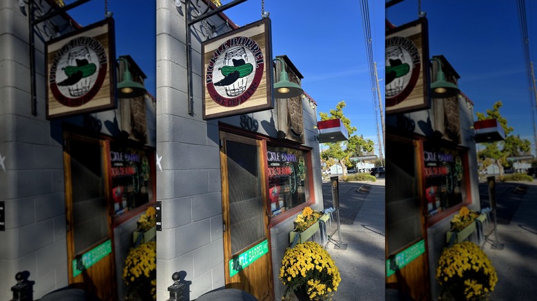 Exterior of Pickle Barrel with hanging sign and yellow potted flowers on sidewalk