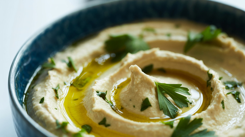 Blue bowl of hummus drizzled with olive oil and topped with herbs