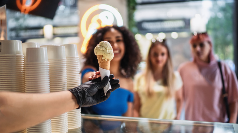 Woman accepting a vanilla ice cream cone from the gloved hand of a worker