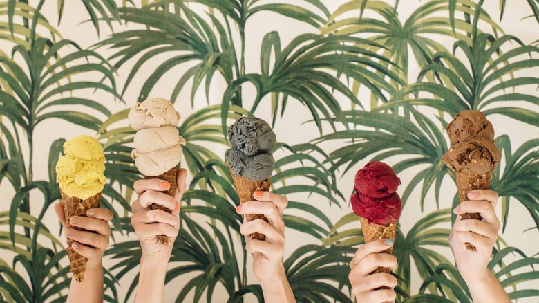 Frankie & Jo's artsy photo with hands holding various ice cream cones in front of wallpaper with foliage