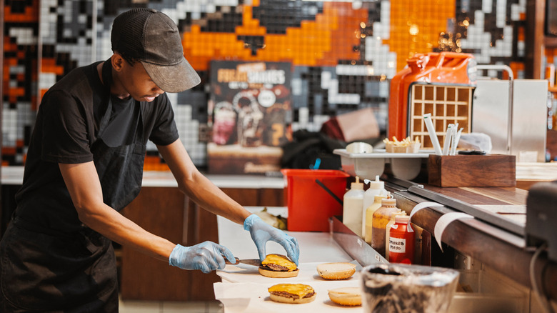 A worker assembling a cheeseburger inside of a fast food restaurant.