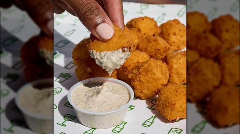 A person dipping the Mac and Cheese Bites from Shake Shack into a creamy sauce