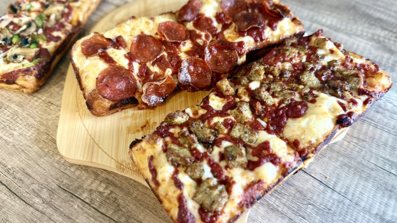 Three Detroit-style pizzas from Domino's with different types of ingredients on each.