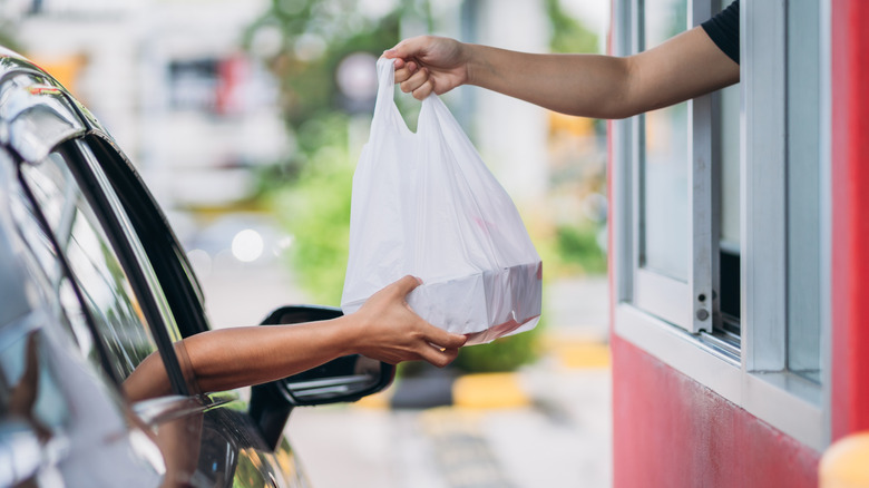 A fast food drive-thru worker handing a plastic bag to someone in their car.