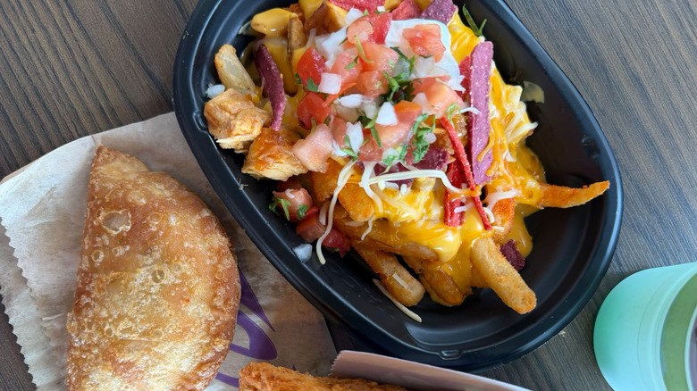Loaded fries in a black takeout container, topped with cheese, nacho strips, and pico de gallo