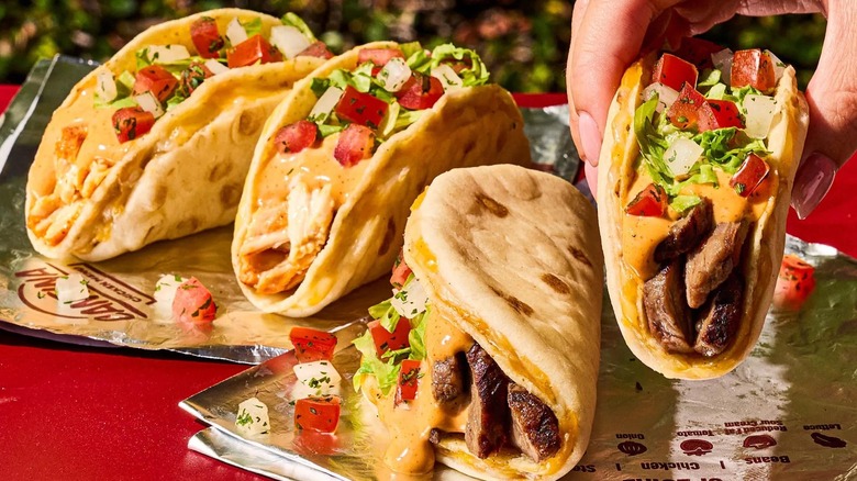 Three mini, taco-shaped Gordita Crunch Duos on Taco Bell packaging while a fourth is picked up