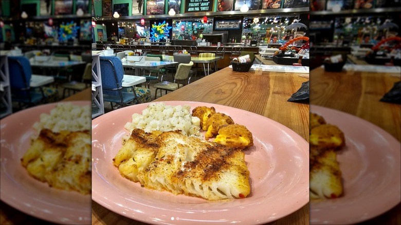 White fish with blackened seasoning, potatoes, and hot honey cheesy bites plated with Interior dining area in background with retro decor at Remember When Cafe