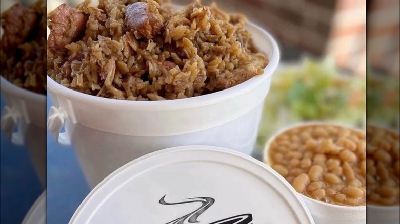 Jambalaya in a takeout container with a lid in front of it and a side of beans in the background at The Jambalaya Shoppe