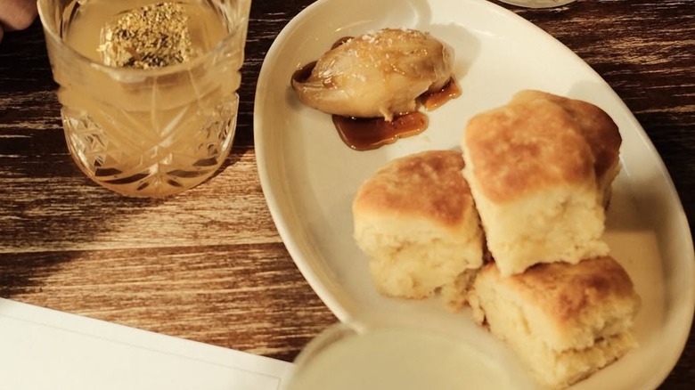 Angel biscuits served with sea-salted, whipped cane syrup butter sitting on table beside a drink