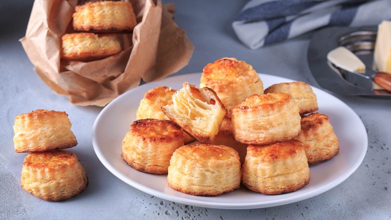 Flaky, textural biscuits on a white plate, with a paper sack of biscuits in background