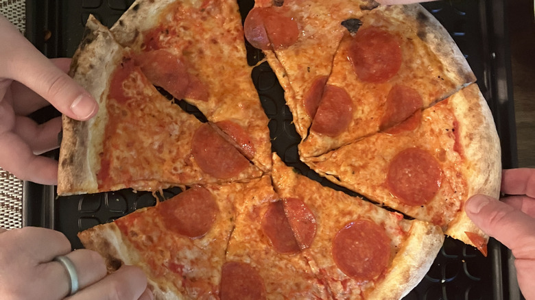 Hands reaching in for slices of frozen and prepared pepperoni pizza.
