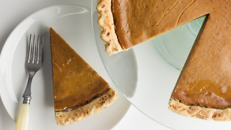 Store-bought pumpkin pie with one slice missing alongside a white plate with one piece of pumpkin pie