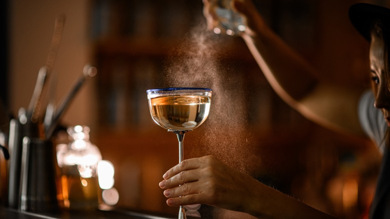Cocktail glass with a tall metal stem being poured by a bartender at a bar