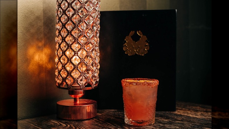 Drink on a table with nice lamp lighting alongside and a menu in background at The Velveteen Speakeasy