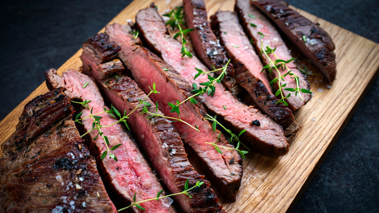Flank steak cut on wooden cutting board revealing its interior, with thyme sprigs on top.