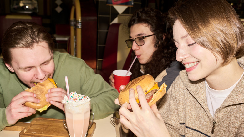 Three young people eating burgers and shakes from a fast food restaurant.