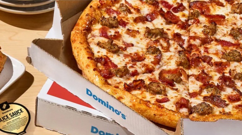 A sausage pizza in a Domino's box sitting on top of another pizza box on a table.