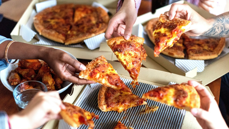 Several hands holding slices of pizza over delivery boxes on a table.