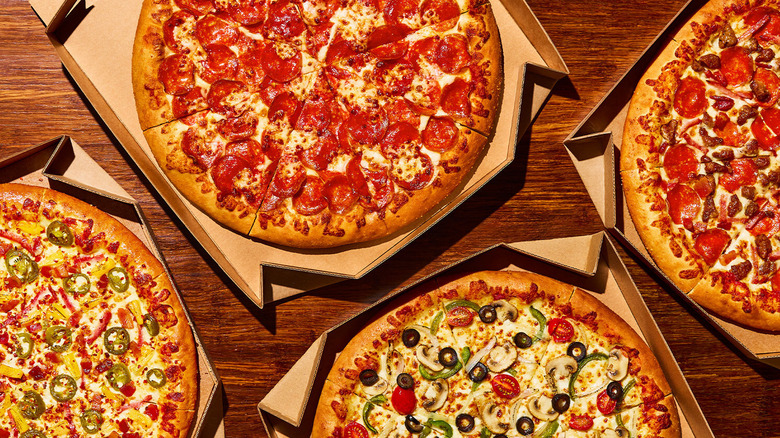 An array of Pizza Hut pizzas inside pizza boxes on a wood surface.