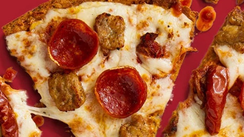 A cauliflower crust sausage and pepperoni pizza from Topper's on a red background.