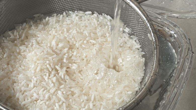 Large sifter filled with dried rice being rinsed with running water