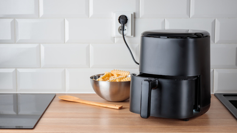 A black air fryer on a kitchen counter plugged into a power socket