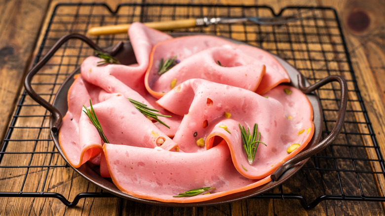Top view of mortadella sausage slices with pistachios for sandwiches in steel tray on wooden background.