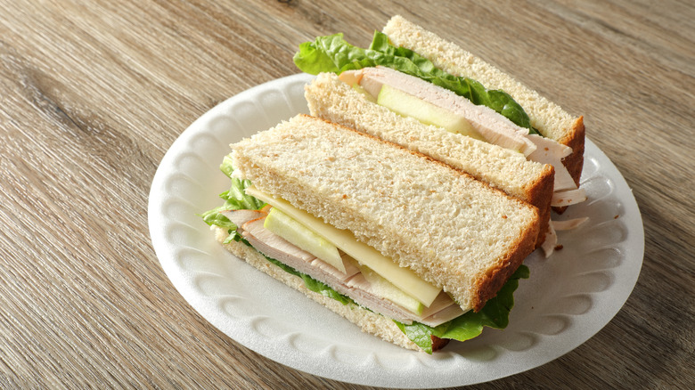 Close up chicken sandwich with light cheese and lettuce on white bread on white strofoam plate.