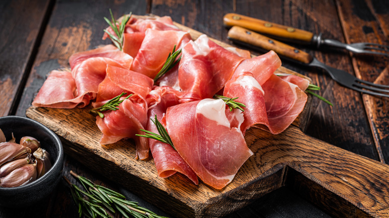 Slices of prosciutto crudo parma on wooden board with rosemary