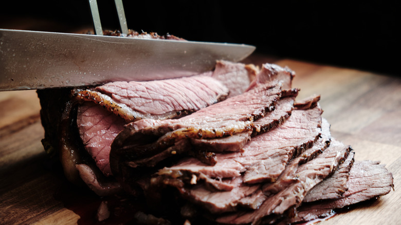 Sliced medium-rare roast beef on a wooden cutting board
