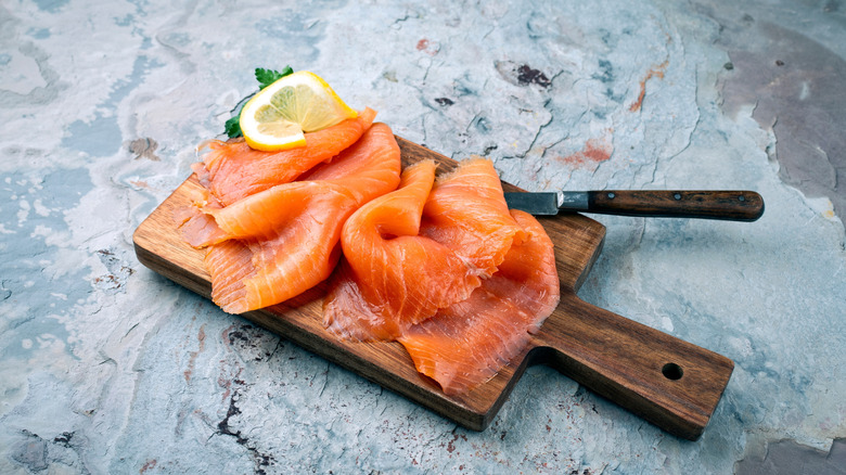 Traditional Norwegian smoked salmon in slices with parsley and lemon served as close-up on rustic wooden chopping board