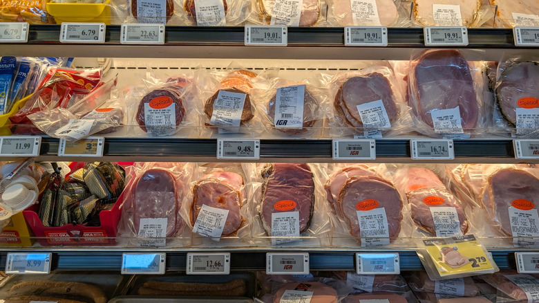 Deli meats and sausages displayed in a brightly lit supermarket cooler