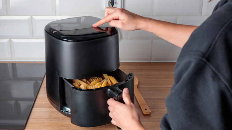 A woman using an air fryer to cook potato wedges at home.