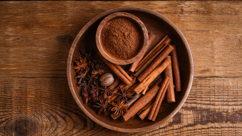 Various spices, including anise seed and cinnamon sticks, in a wooden bowl on a wooden surface