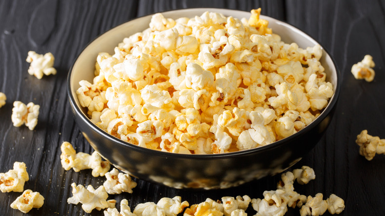 Black bowl full of popcorn with spilled kernels on surface