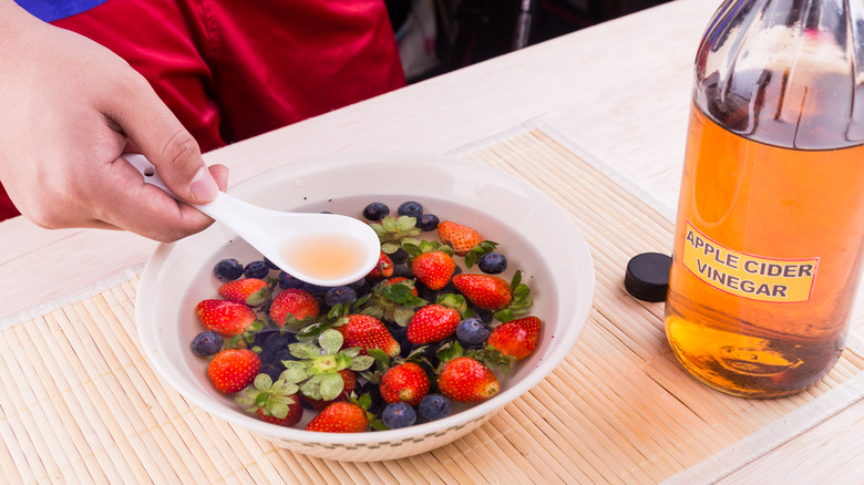 Person applying apple cider vinegar to bowl of berries