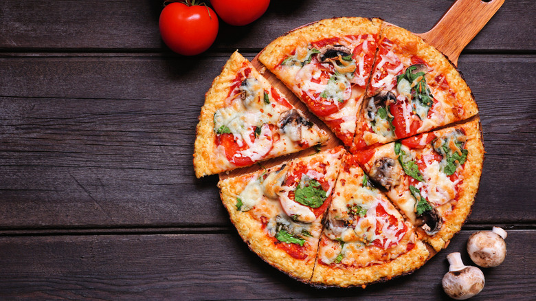 Cauliflower crust pizza on pizza paddle with ingredients nearby.