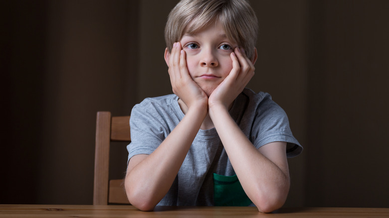 A little boy resting both elbows on table