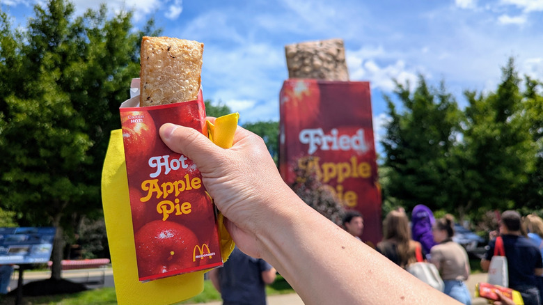 Hand holding McDonald's fried apple pie up against apple pie statue in the background.