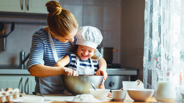 Woman mixing ingredients together in a bowl with her child in the kitchen.