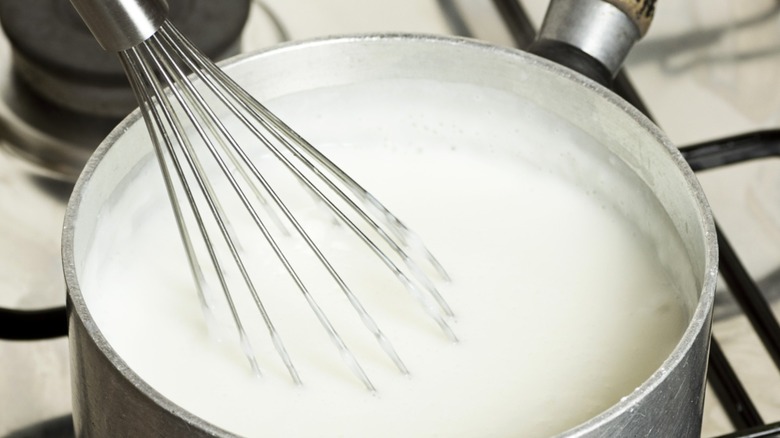 Person whisking cream and cornstarch in pot over stove