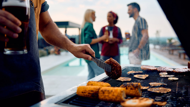 A man grilling with a glass of beer in his hand at an outdoor social gathering.